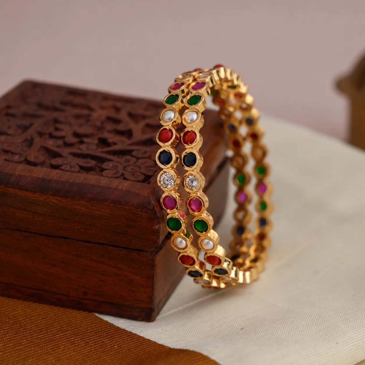 A pair of multicolour gold-tone bangles displayed against a carved wooden box