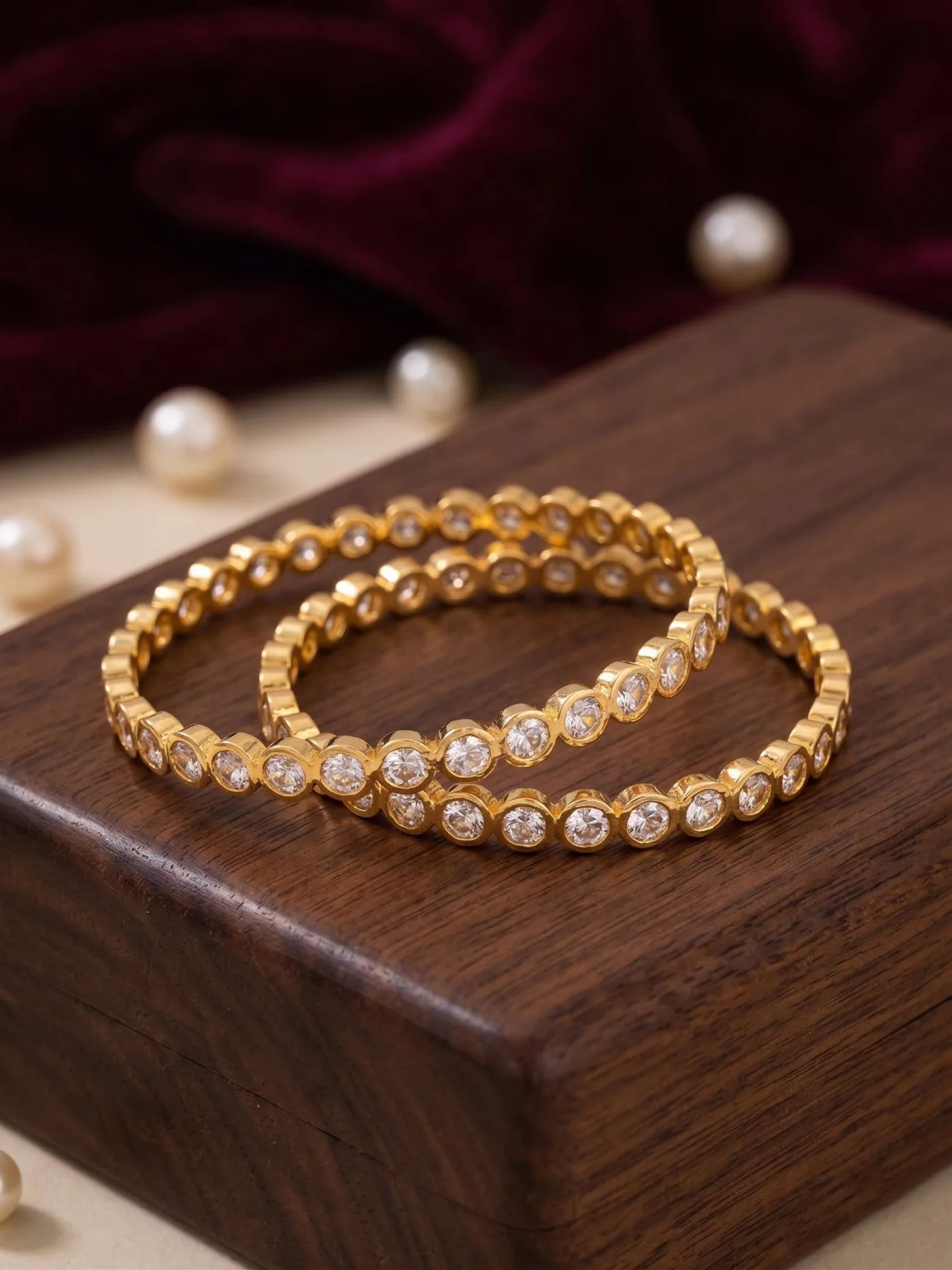 Pair of gold-tone bangles with round white stones arranged on a polished wooden display